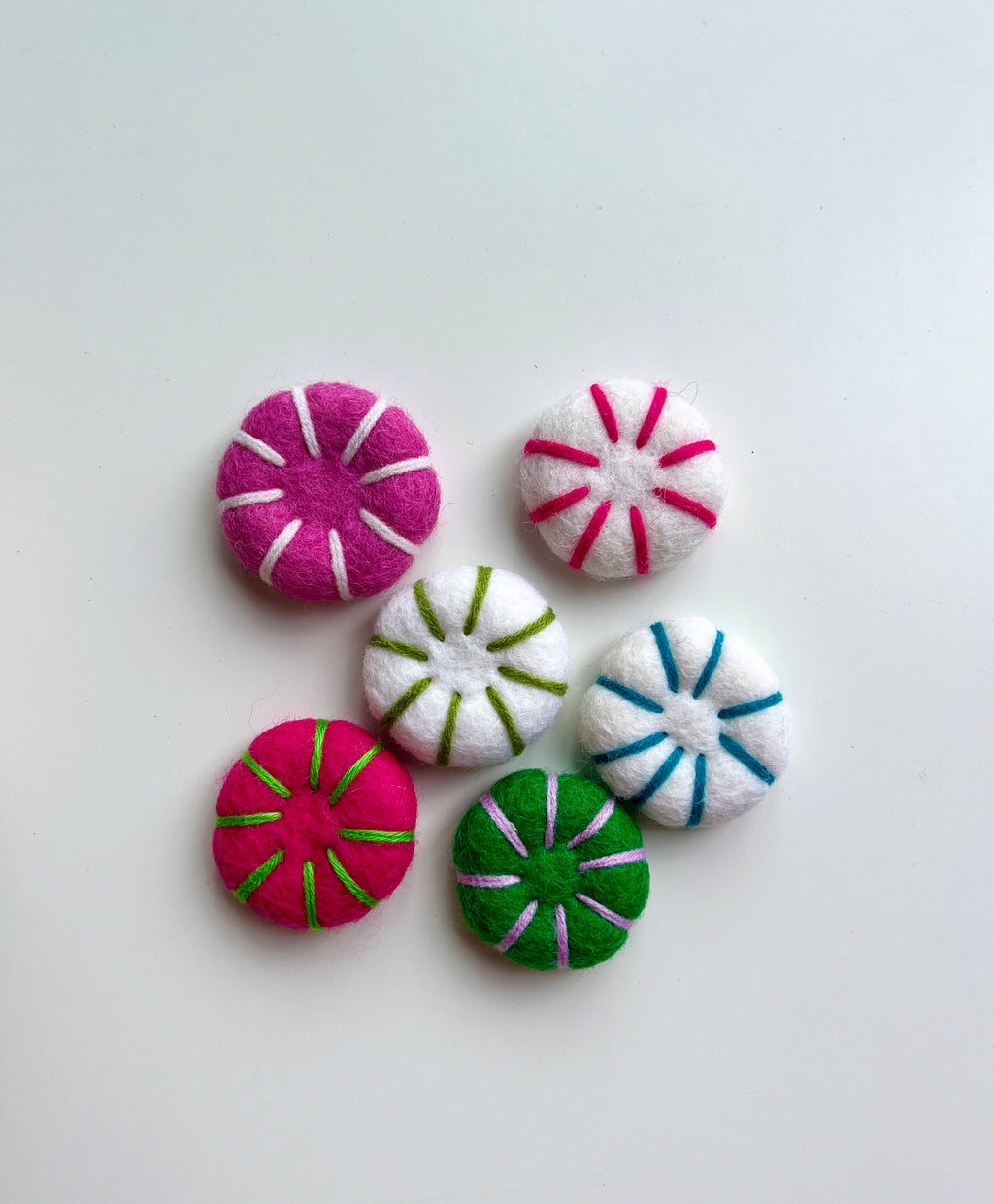Six round felt decorations in pink, green, and white with contrasting stitched lines on a white background
