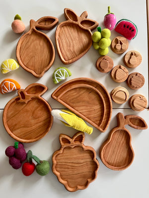 Variety of wooden fruit-shaped trays including orange, lemon, strawberry, watermelon, pear, and grape with felt fruit accents and stamps