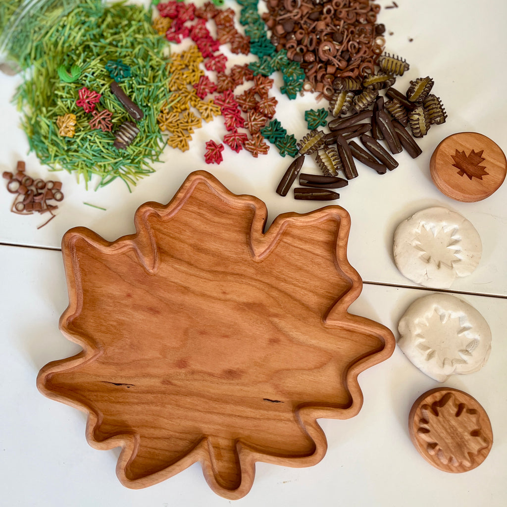 Maple leaf-shaped wooden tray with matching wooden stamps, white clay leaf imprints, and colorful nature-inspired craft materials