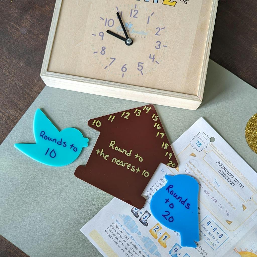 Wooden clock with loose hands, brown house-shaped piece with numbers, and blue bird-shaped pieces labeled with rounding instructions