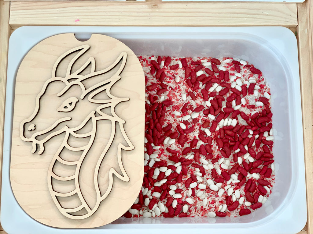 Plastic tub filled with red and white rice with a wooden dragon stencil resting on the edge of the container