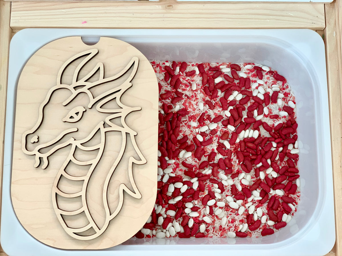 Plastic tub filled with red and white rice with a wooden dragon stencil resting on the edge of the container