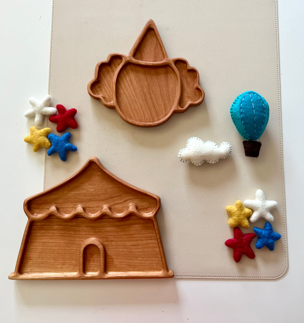 Two wooden trays shaped like a circus tent and clown face surrounded by colorful felt stars, a cloud, and a hot air balloon