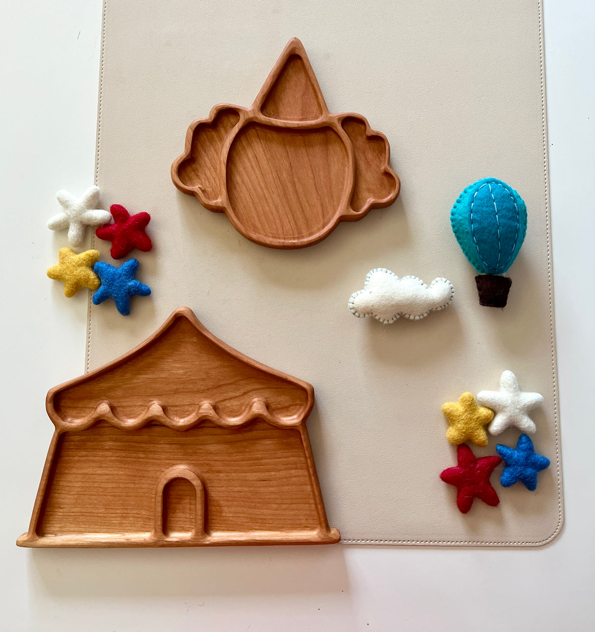 Two wooden trays shaped like a circus tent and clown face surrounded by colorful felt stars, a cloud, and a hot air balloon