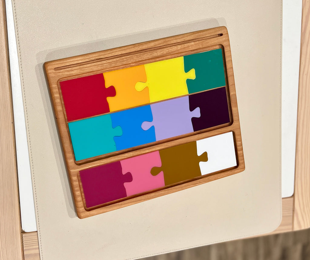 Wooden tray holding three rows of colorful rectangular puzzle pieces in red, orange, yellow, green, blue, purple, pink, brown, and white