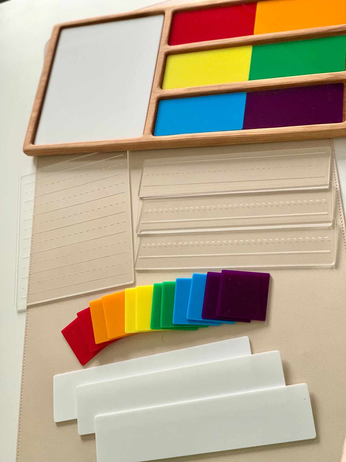Wooden tray with colorful rectangular tiles, clear plastic cards with embossed lines, and white plastic nameplates on a beige surface