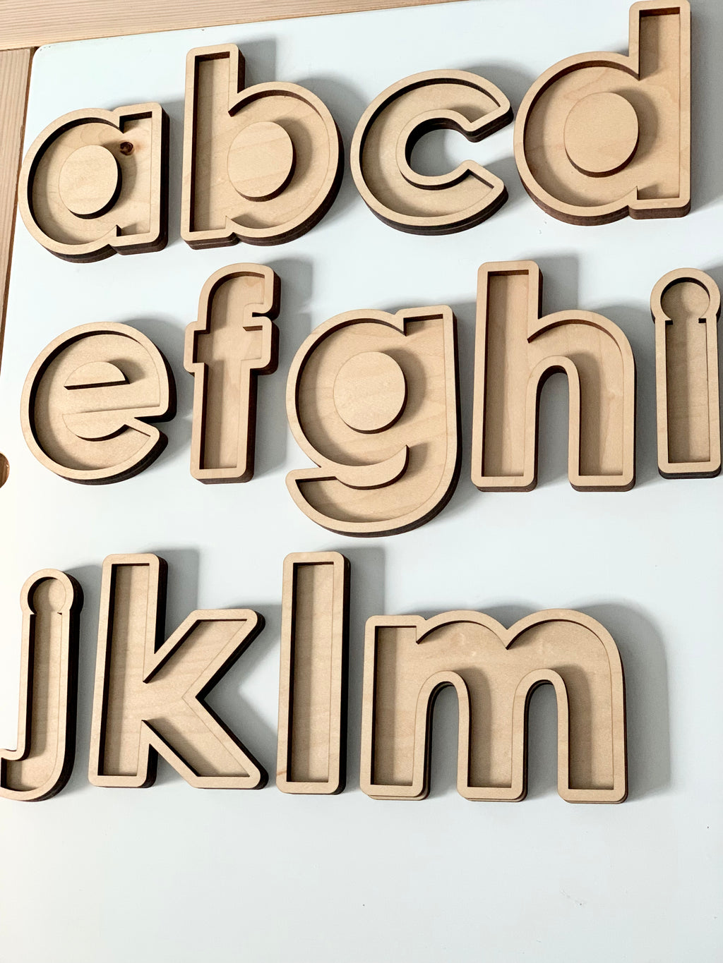 Laser-cut wooden lowercase alphabet trays from a to m arranged on a white background for sensory play.