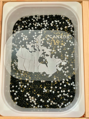 Translucent map of Canada with provincial outlines on a sensory bin filled with black and silver beads and yellow grains