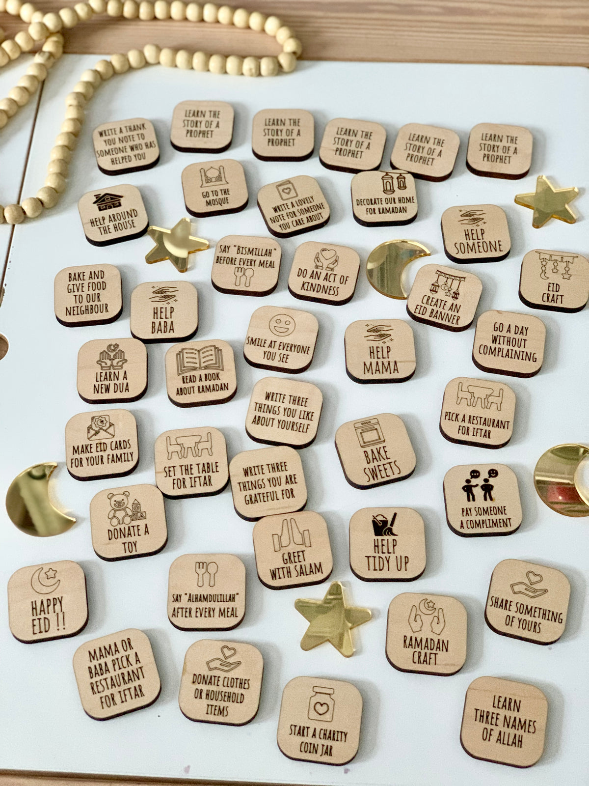 Wooden activity tiles with engraved Ramadan and Eid-themed tasks and icons arranged on a white surface with decorative stars and beads