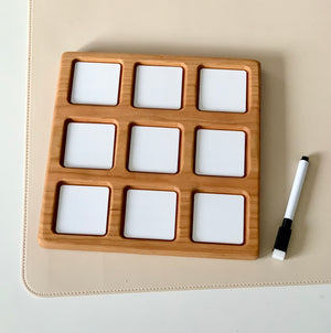 Wooden 3x3 tic tac toe grid with white dry erase squares and black dry erase marker on beige surface