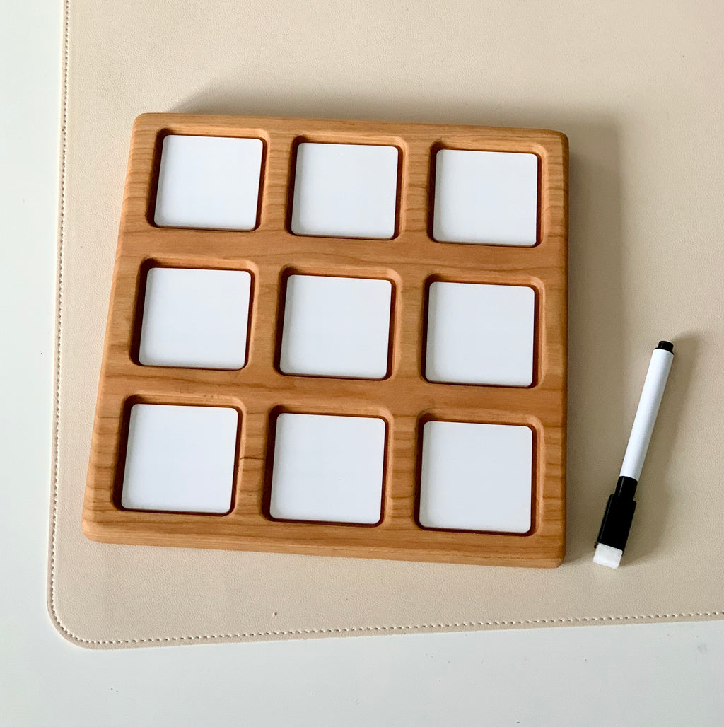 Wooden 3x3 tic tac toe grid with white dry erase squares and black dry erase marker on beige surface