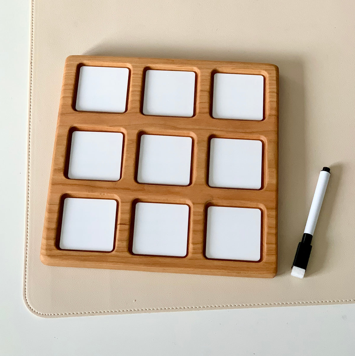Wooden 3x3 tic tac toe grid with white dry erase squares and black dry erase marker on beige surface