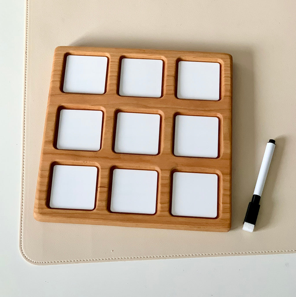 Wooden board with nine square white dry erase tiles arranged in a 3x3 grid next to a black and white marker
