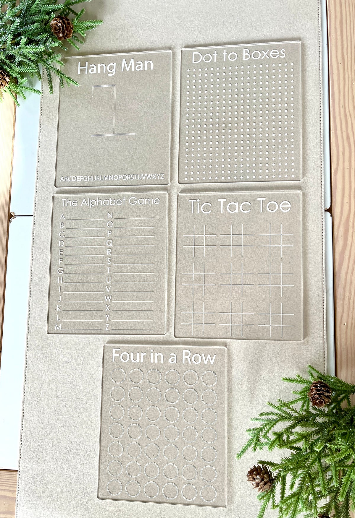 Set of five clear acrylic game boards for Hangman, Dot to Boxes, Alphabet Game, Tic Tac Toe, and Four in a Row on a beige mat
