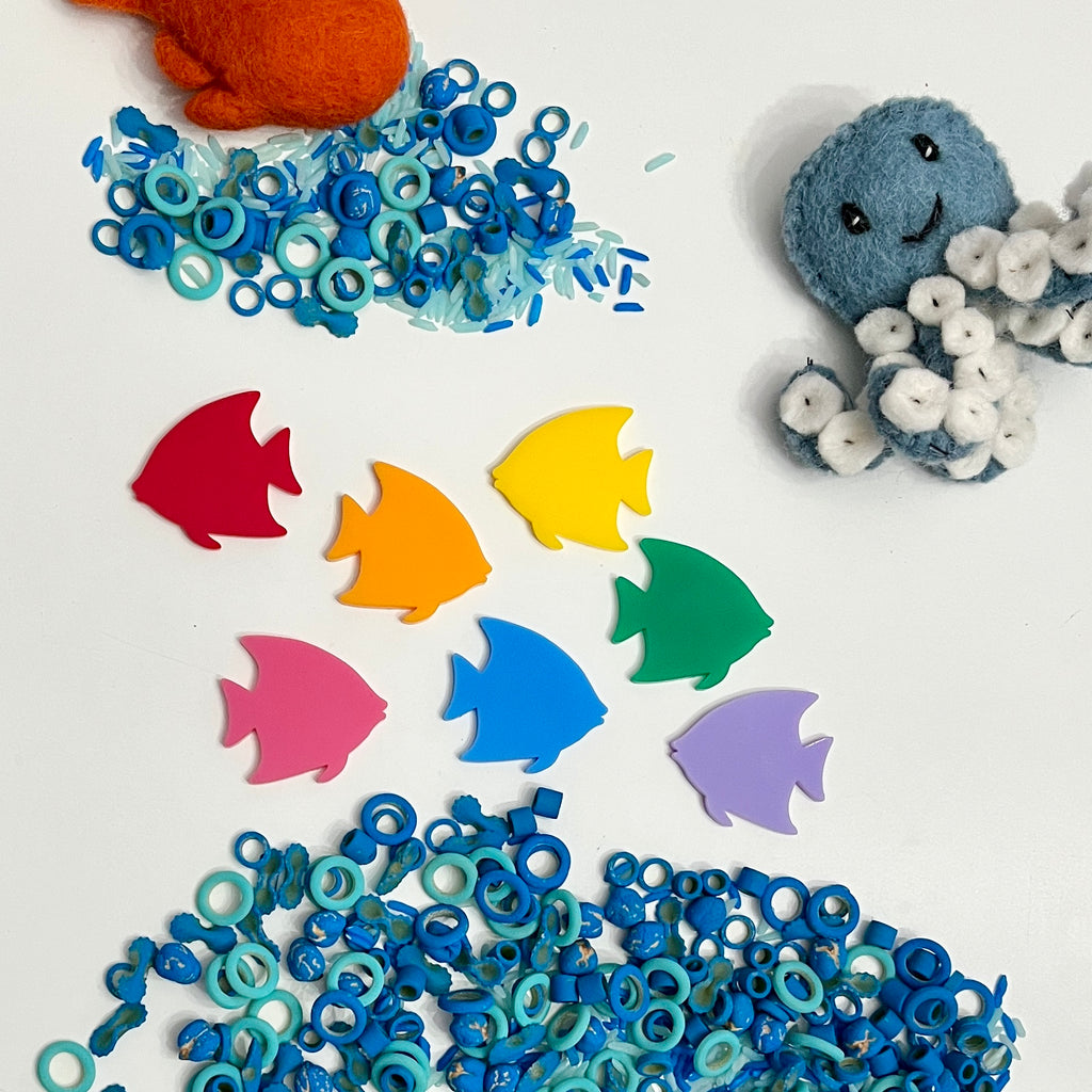 Colorful acrylic fish shapes with scattered blue ring beads and felt octopus and crab on white background