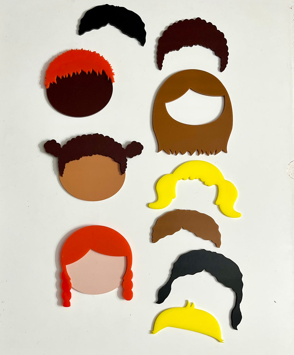 Colorful flat face and hair shapes in diverse styles and shades arranged on a white background