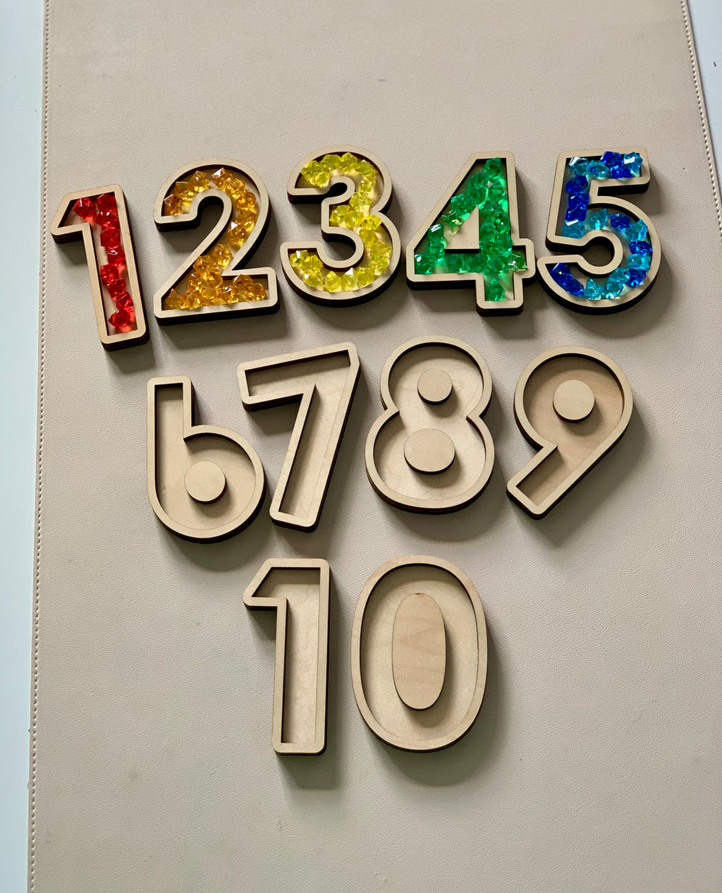 Wooden number cutouts with colorful translucent beads inside numbers 1 to 5 and plain wooden 6 to 10 on beige surface