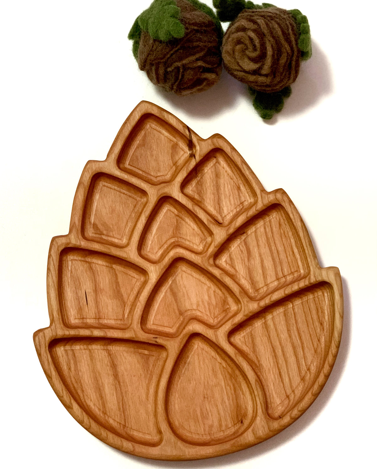 Light wood tray with multiple geometric compartments shaped like a pinecone alongside two felted brown flowers with green leaves