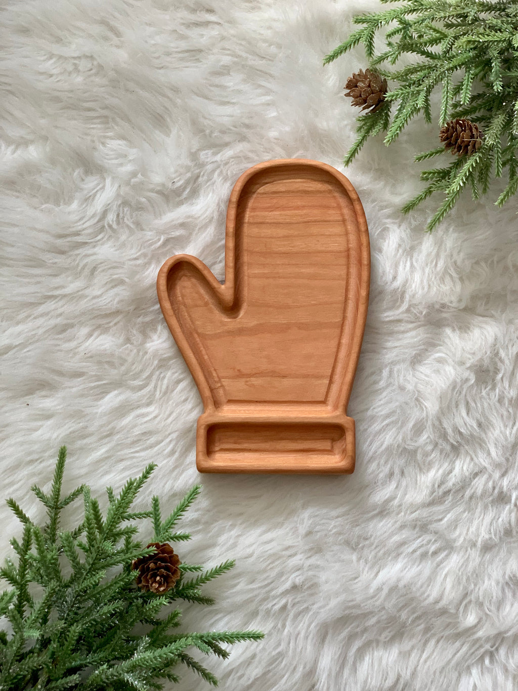 Wooden mitten-shaped sensory tray on fluffy white surface with pinecones and evergreen sprigs nearby