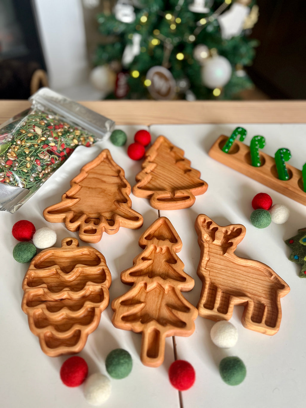 Wooden baking molds shaped like pinecone, Christmas trees, and a reindeer on white surface with holiday decor nearby