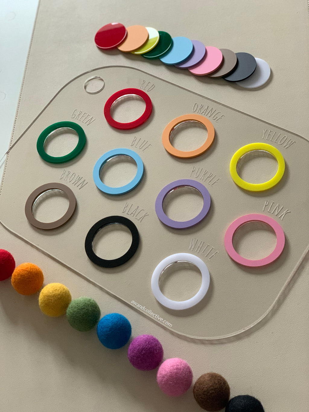Clear acrylic color chart with labeled colored rings and matching solid color discs on a light surface with felt balls below