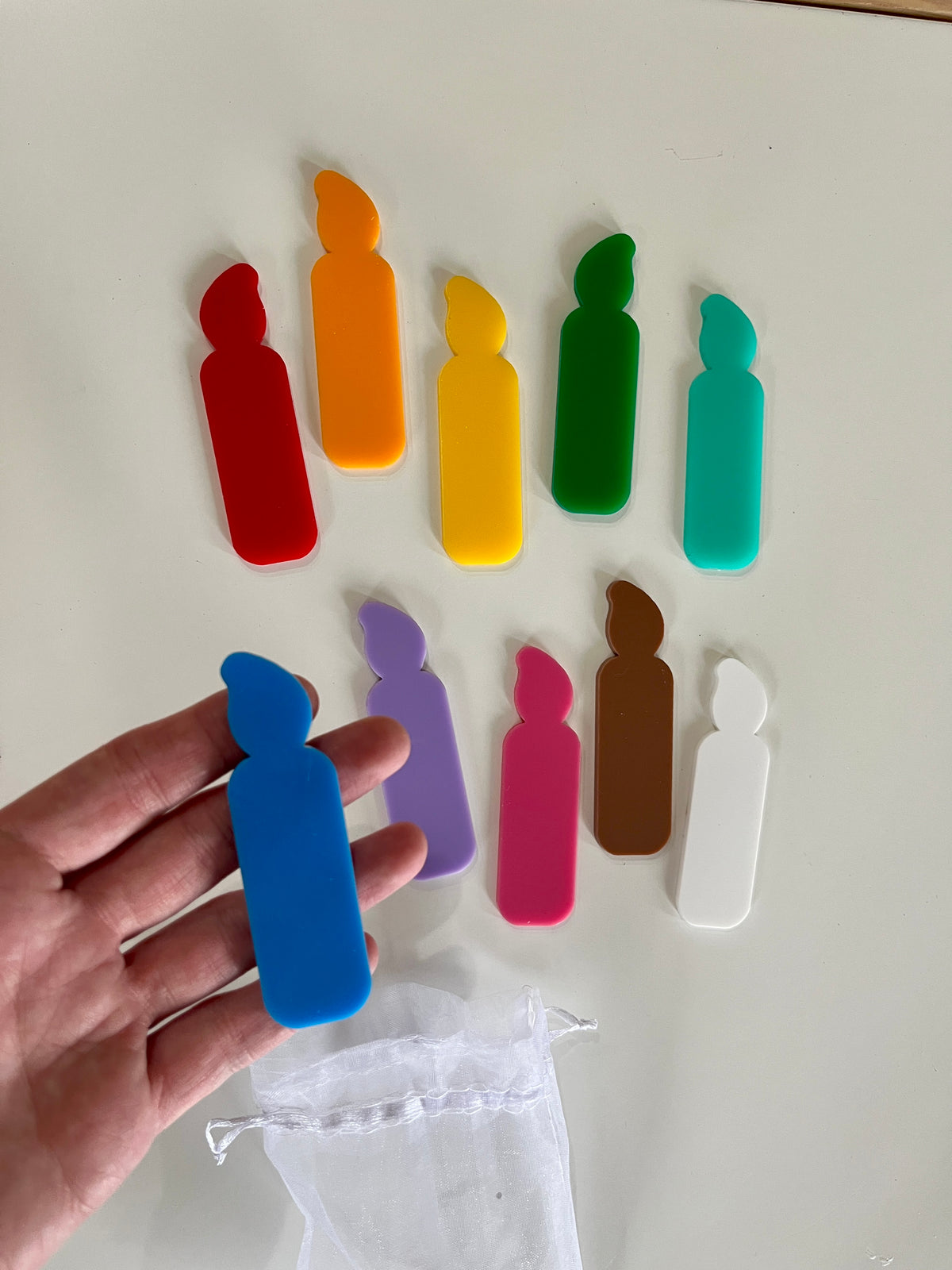 Set of colorful flat candle-shaped tokens in red, orange, yellow, green, teal, blue, purple, pink, brown, and white with a white drawstring pouch