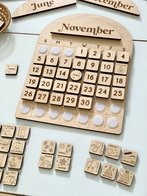 Wooden perpetual calendar board with interchangeable date tiles, month panels, and illustrated event markers on white surface