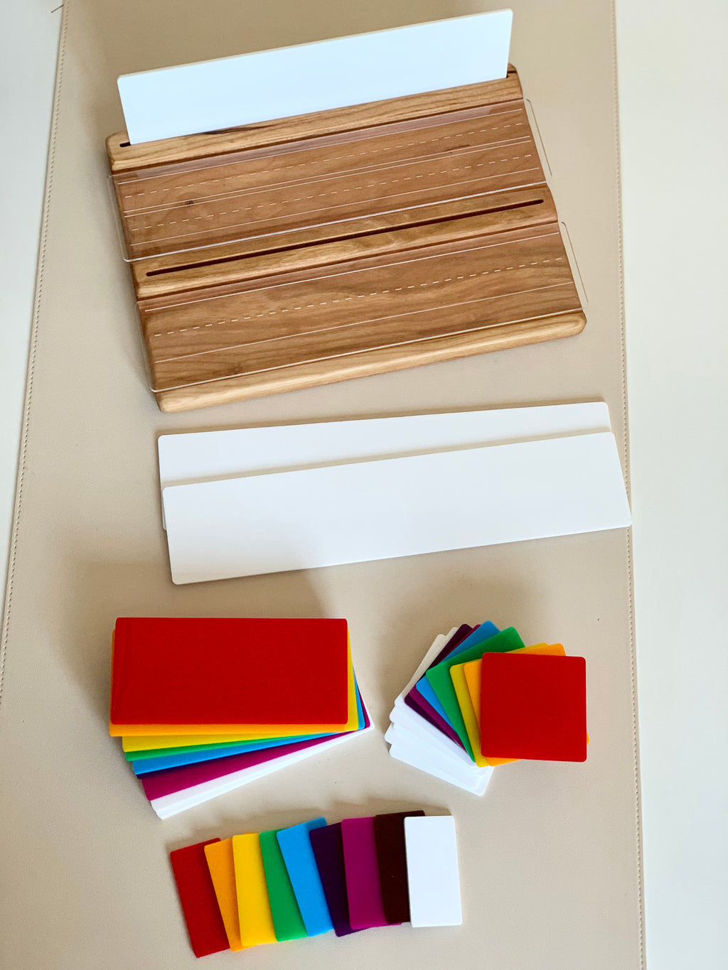 Wooden writing tray with clear dry erase cover, white language boards, and colorful plastic shaped cards on beige surface