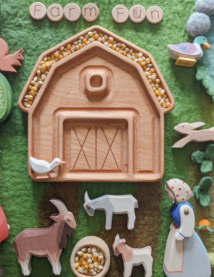 Wooden farm-themed playset featuring a barn tray filled with corn kernels, animals, and a figure on green felt background