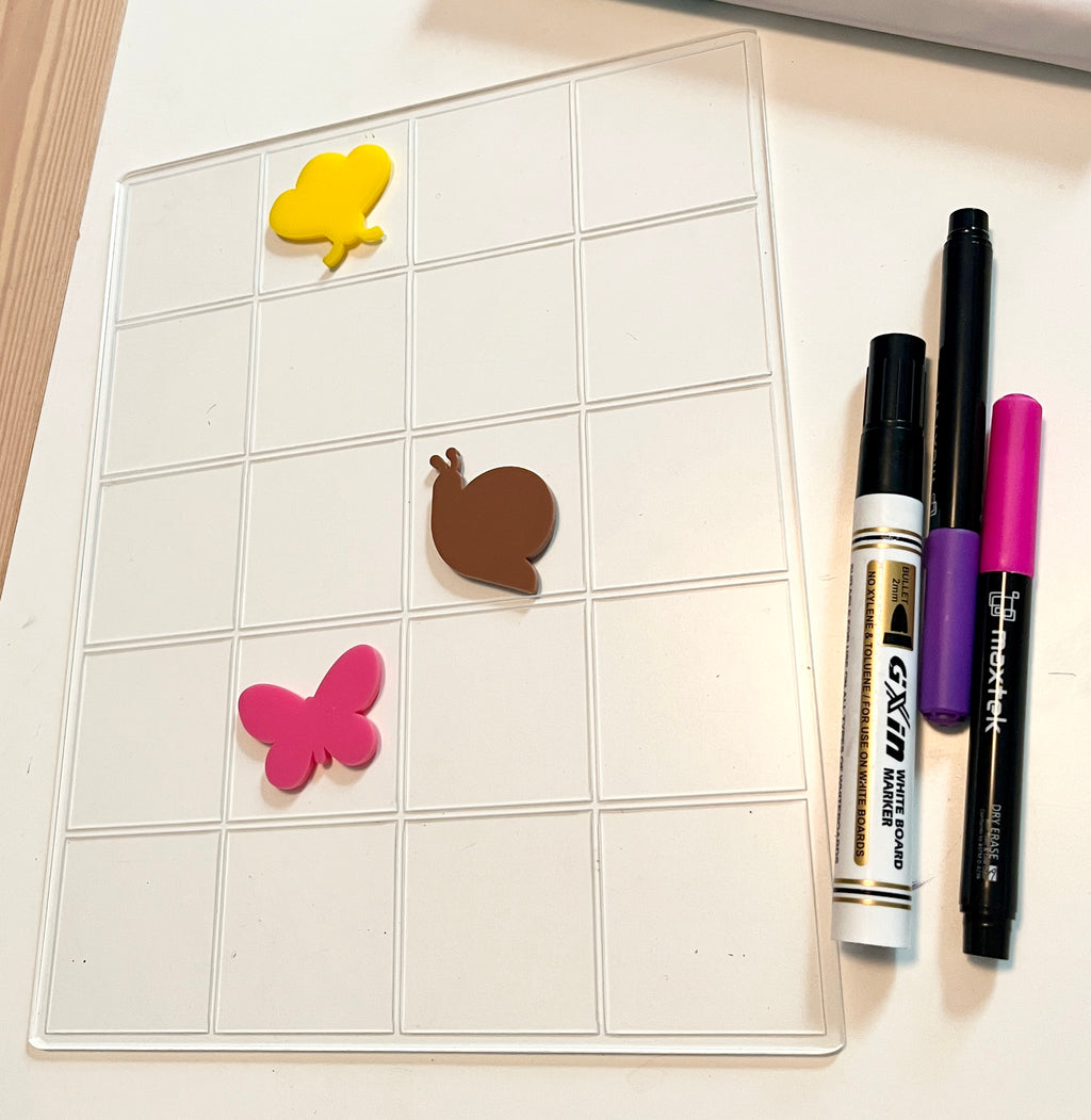 Clear Dry Erase whiteboard with 20 squares, a 20 frame.  It has dry erase bugs sitting on top of it.  