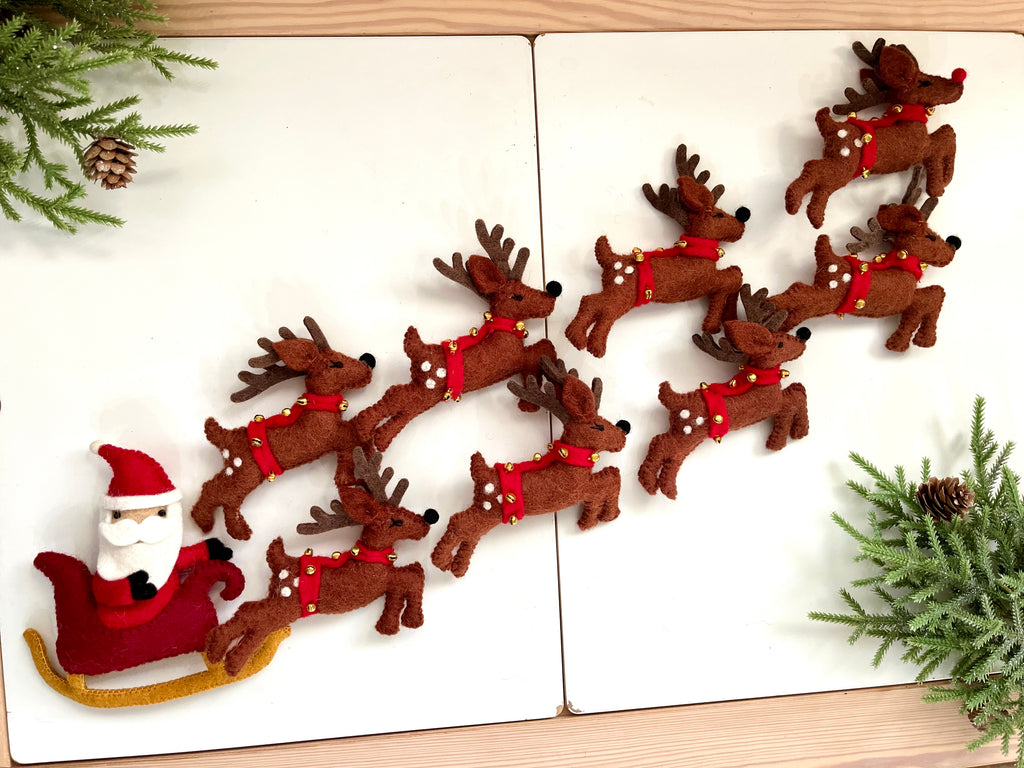 Felt Santa figure in red sleigh being pulled by eight brown felt reindeer with red collars and bells on white surface