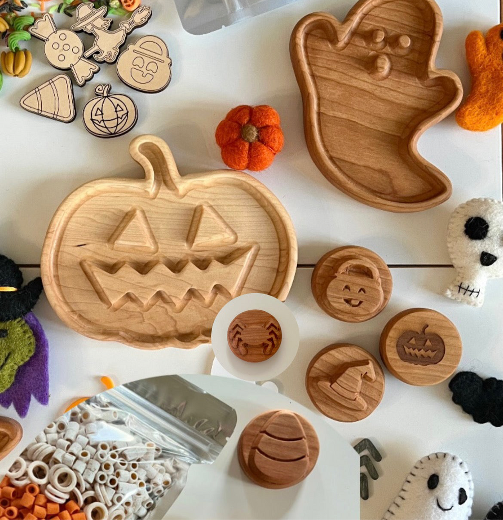 Wooden Halloween-themed trays and round tokens with pumpkin, witch hat, spider, and jack-o’-lantern designs on white surface.
