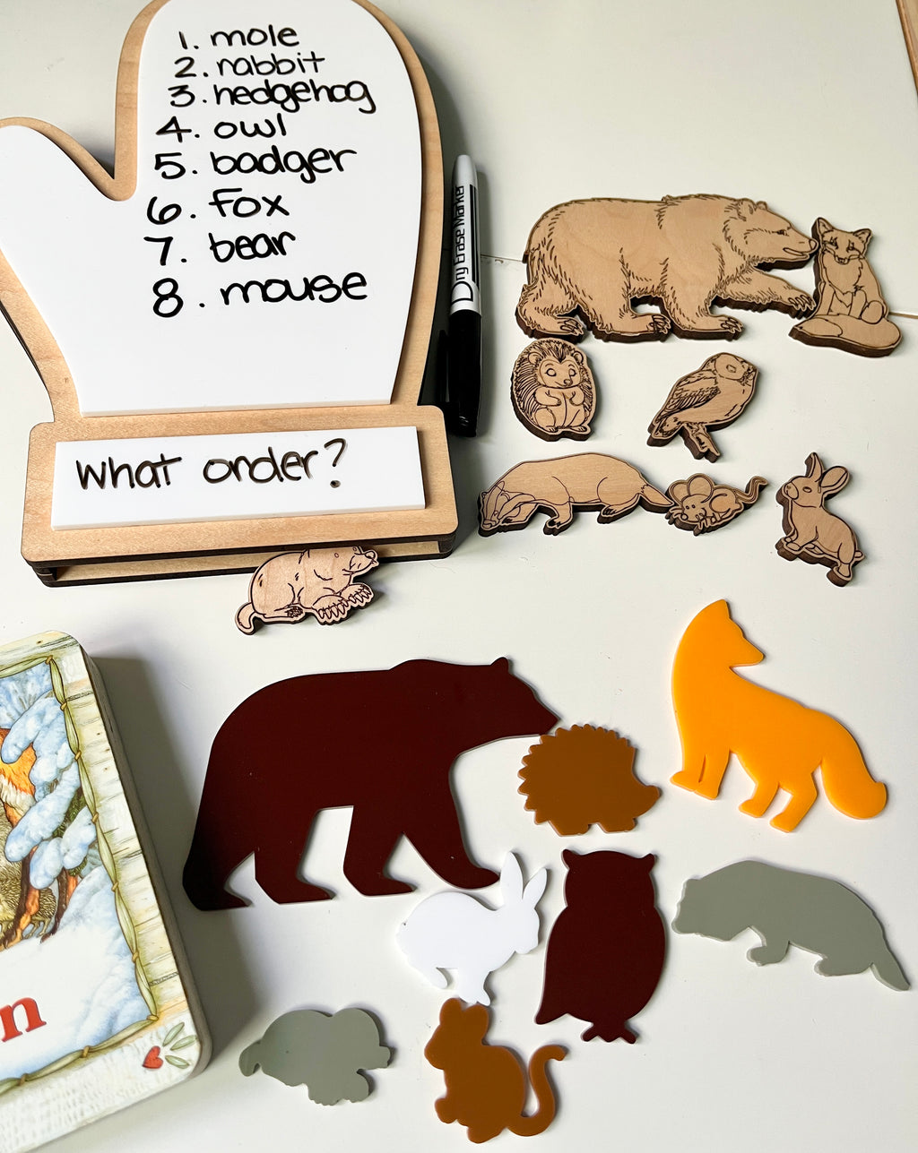 The Mitten Wooden Animals and/or Little Dry Erasables with Mitten Interactive Learning Set showcasing handcrafted wooden animal pieces, colorful silhouettes, a mitten-shaped dry-erase board with handwritten animal names, and a dry-erase marker, unique homeschool education resources.