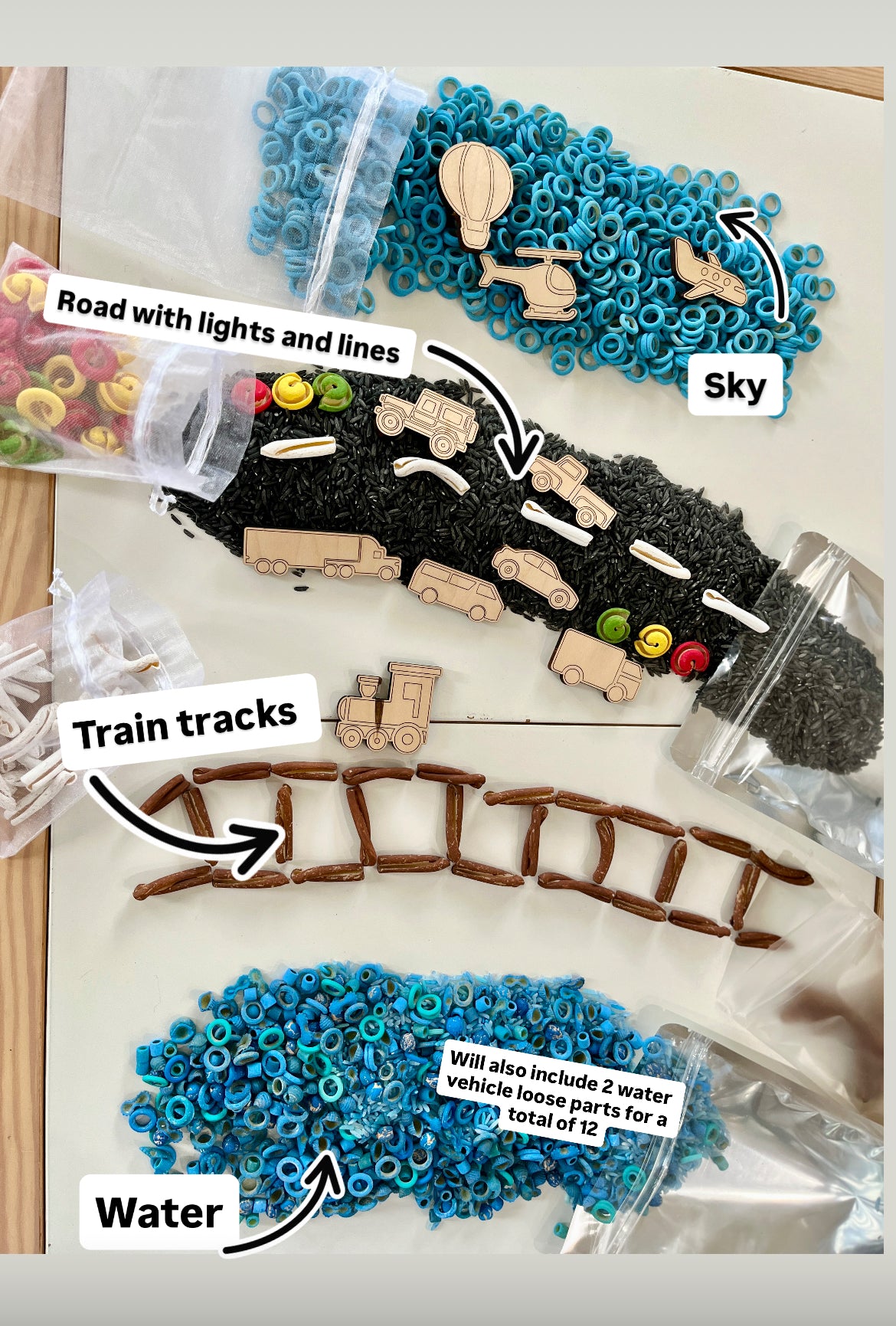 Wooden transportation shapes including train, car, truck on black rice road, blue rings for water and sky, and brown sticks for train tracks