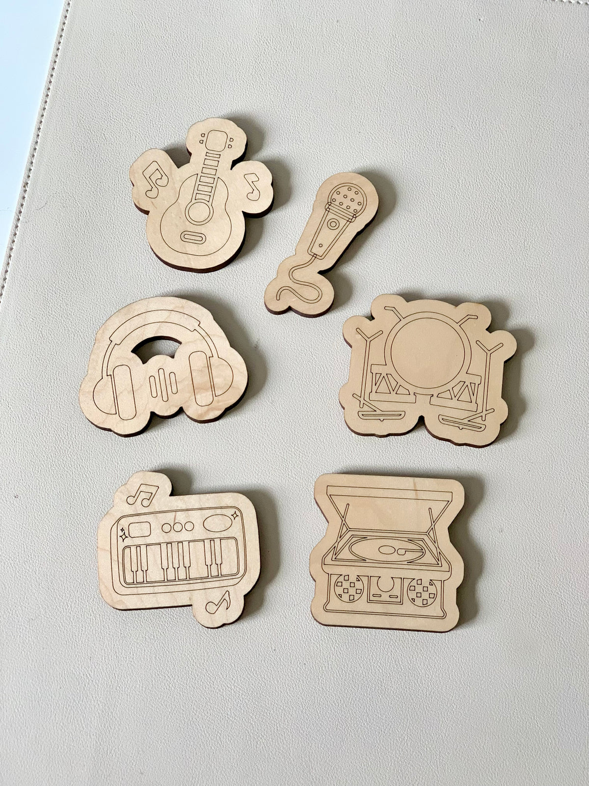 Six wooden music-themed tokens featuring guitar, microphone, headphones, drum set, keyboard, and record player illustrations on a light surface