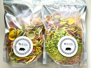 Two clear silver-topped bags filled with colorful dried botanical and snack mix pieces on white surface