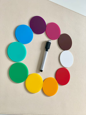 Brightly colored round acrylic discs arranged in a circle with a black and white dry erase marker in the center on a beige surface