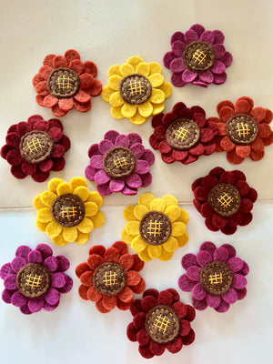 Felt flowers in shades of purple, yellow, red, and orange with stitched brown centers arranged on a light surface
