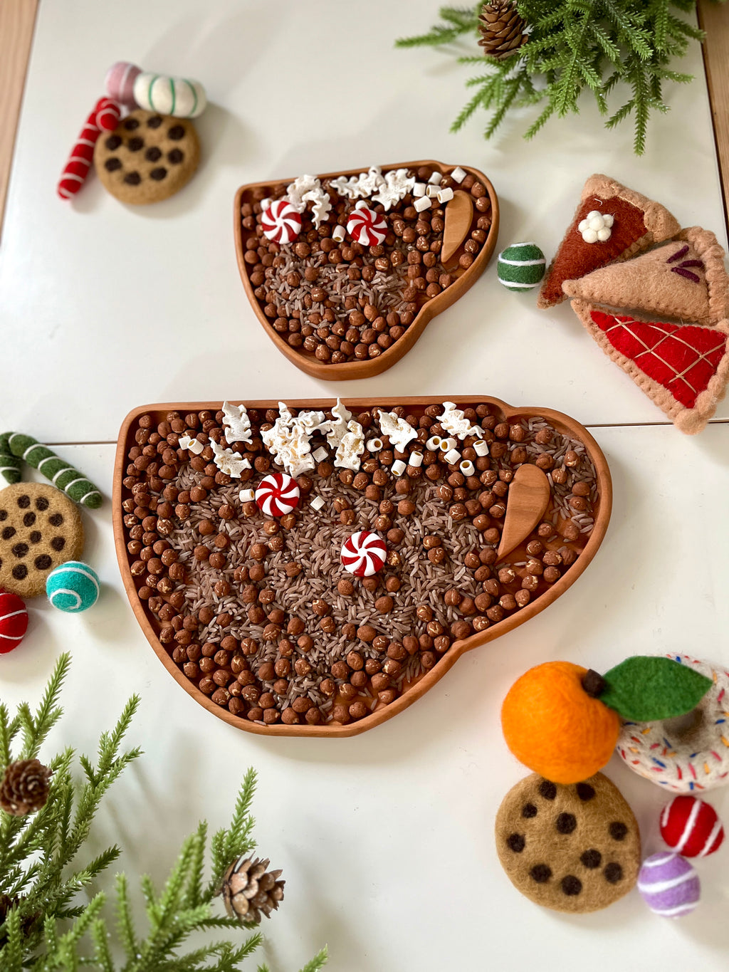 Two wooden trays shaped like coffee cups filled with chocolate beads, popcorn, peppermint candies, and small wooden scoops