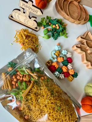 Assorted fall-themed craft items including wooden pumpkin trays, colorful pasta, miniature pumpkin pieces, and chickpeas on white surface