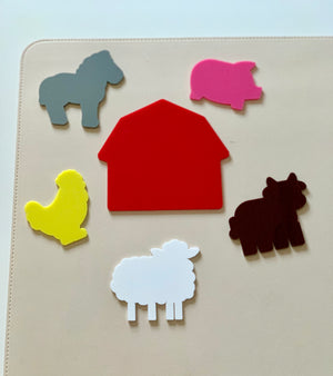 Colorful felt farm animal shapes and a red barn arranged on a light beige surface