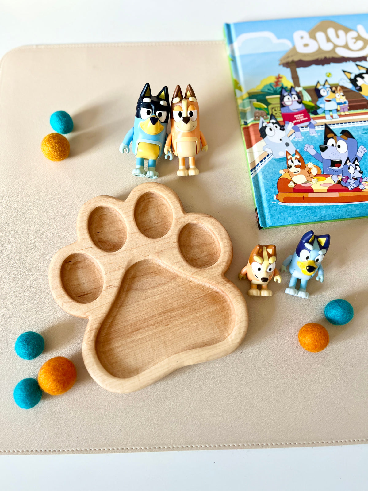 Wooden tray shaped like a dog paw surrounded by colorful felt balls, two dog character toys, and a children's storybook