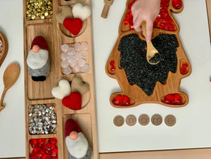 Wooden sensory tray shaped like a gnome with colored rice and small heart decorations on white surface
