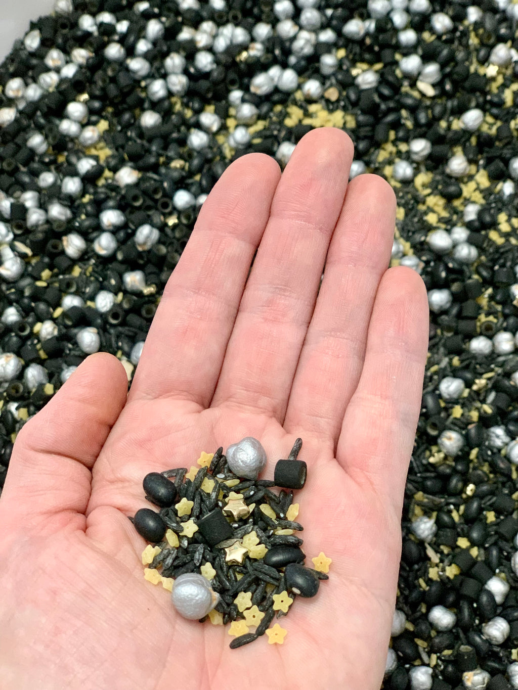 Hand holding black, silver, and gold sensory beads with star shapes over a large tray of similar beads