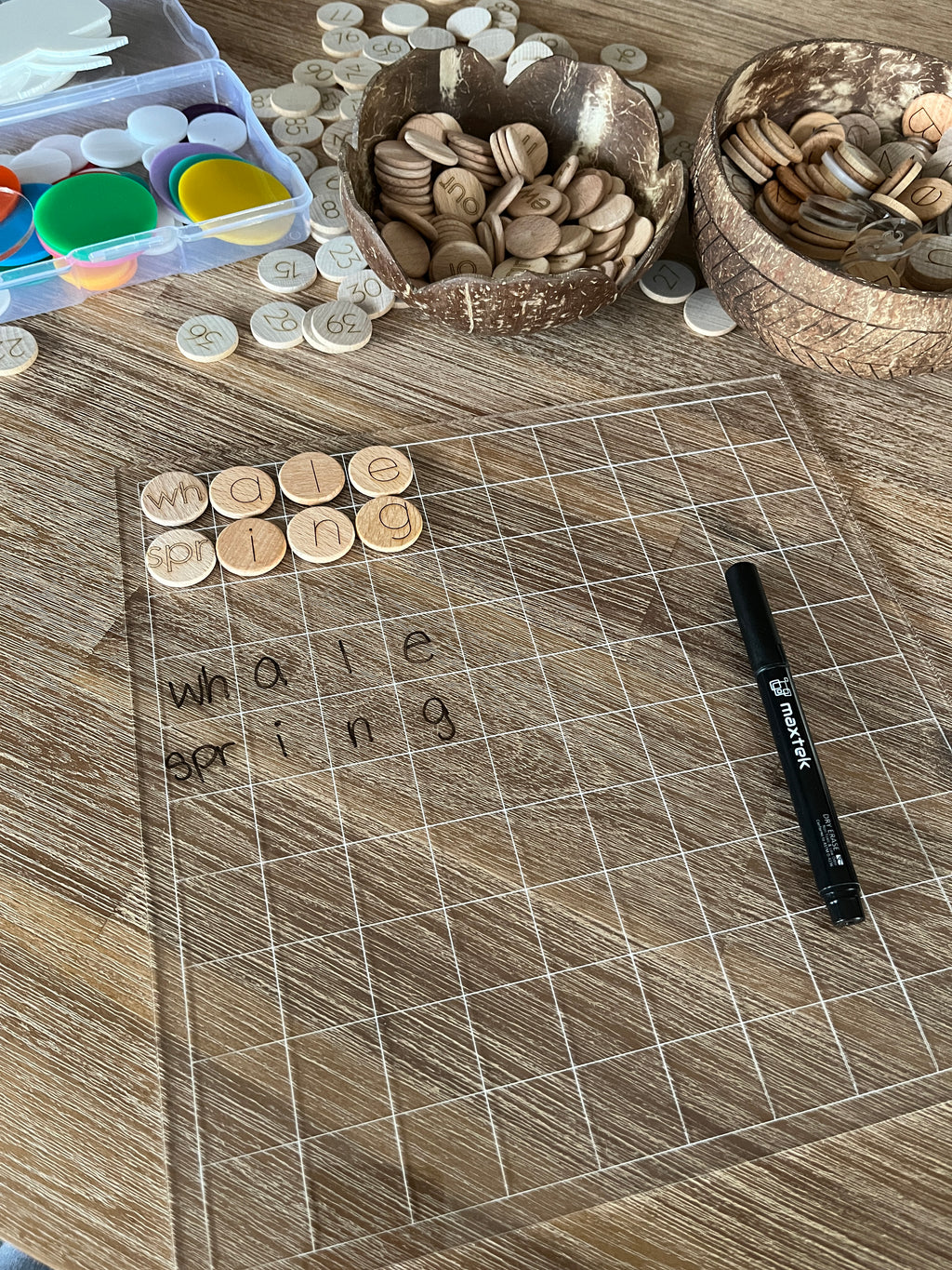 Dry Erasable Blank Open Ended 100 Frame Hundred Board on wood table with clear grid, wooden letter discs spelling simple words, black dry erase marker, handcrafted homeschool education resources.