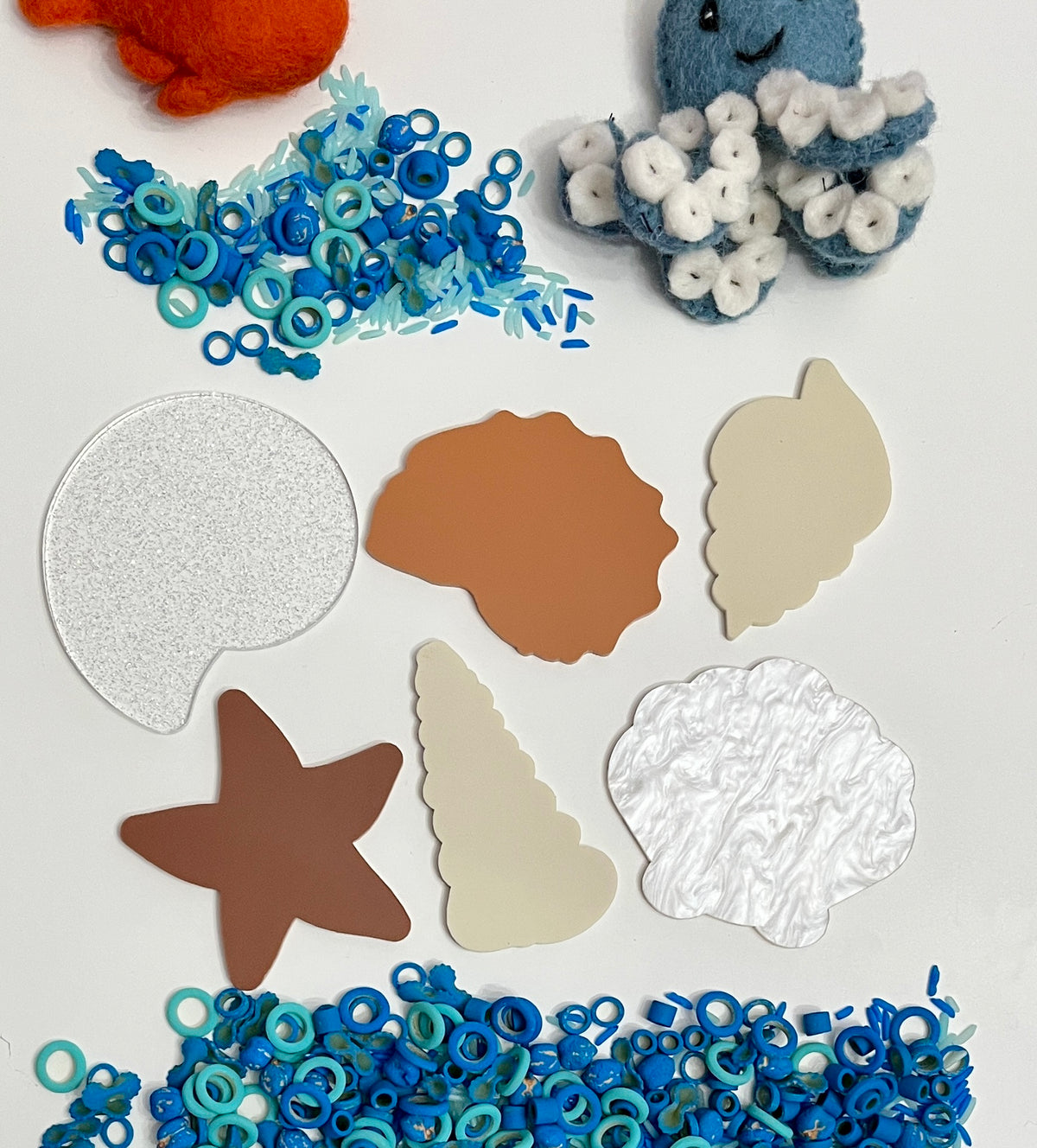 Brown starfish, cream and brown seashell shapes, pearly textured coral piece, blue ring beads, and felt sea creatures on white background