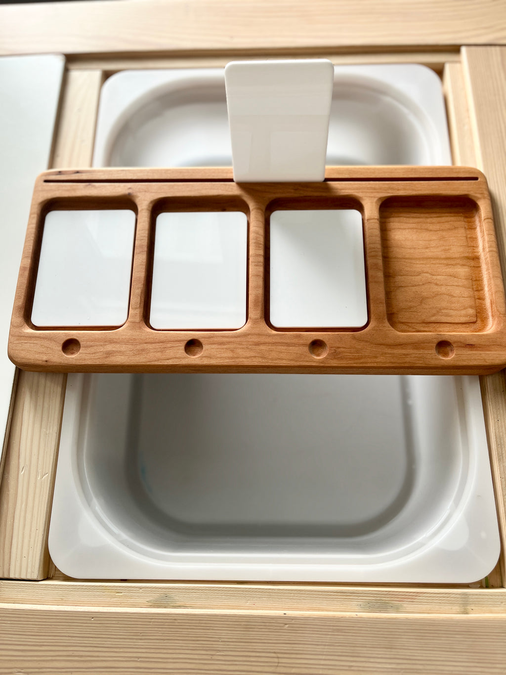 Rectangular wooden organizer with four compartments resting on a white surface with a vertical white plastic handle in the center