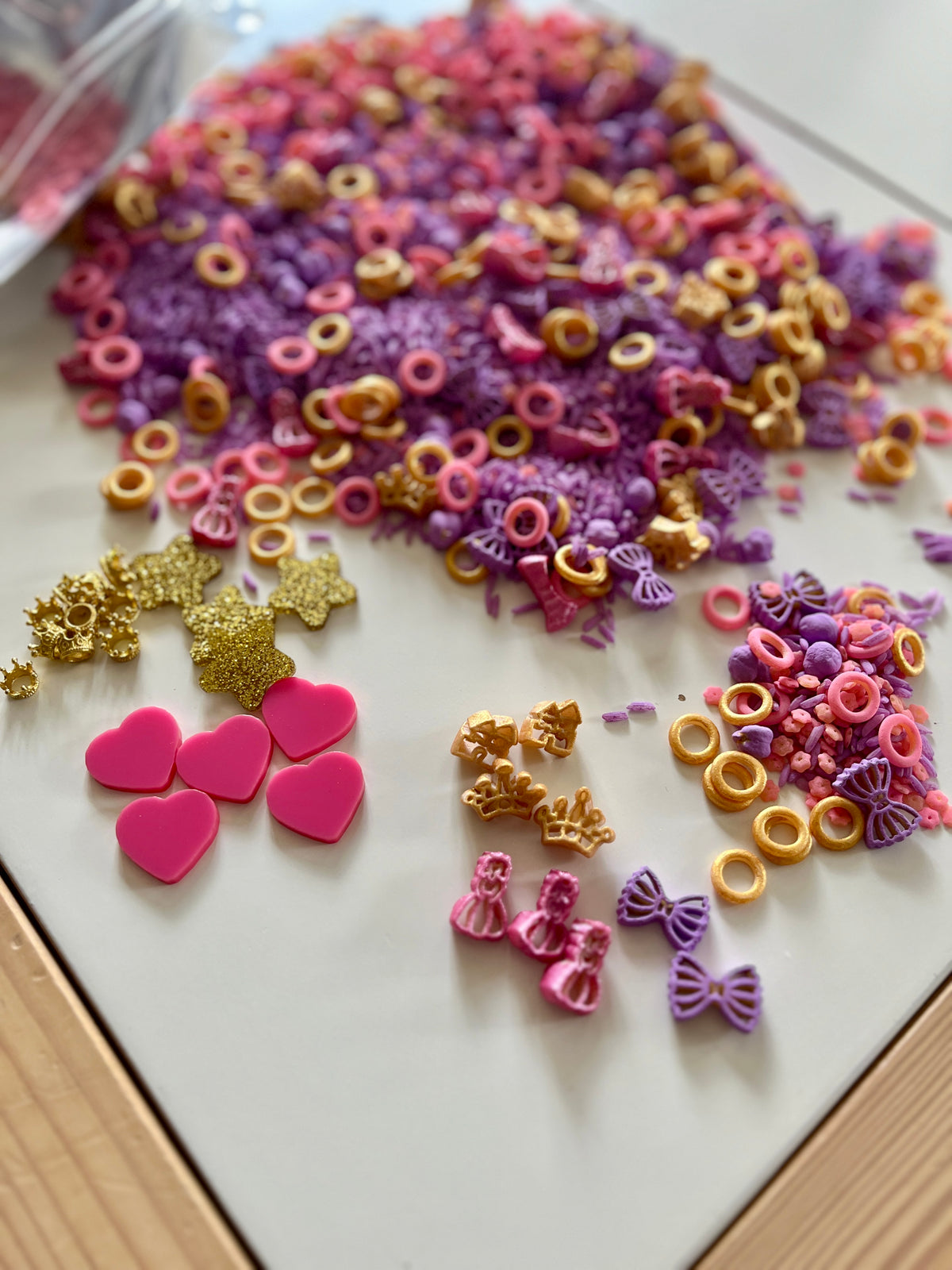 Princess-themed sensory kit with loose parts including pink hearts, gold crowns, bows, and pastel-colored tiny shapes on white surface