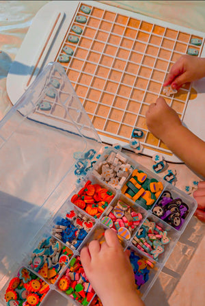 Child placing small colorful wooden pieces into a white grid tray next to a divided plastic organizer container.