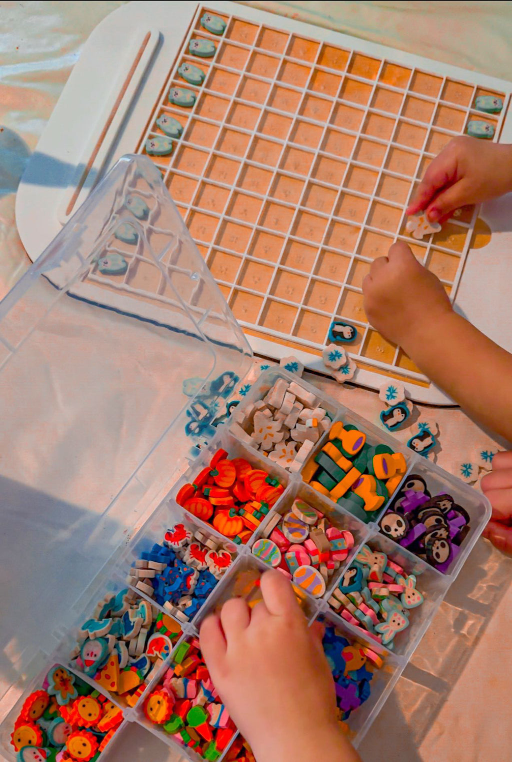 Child placing small colorful wooden pieces into a white grid tray next to a divided plastic organizer container.